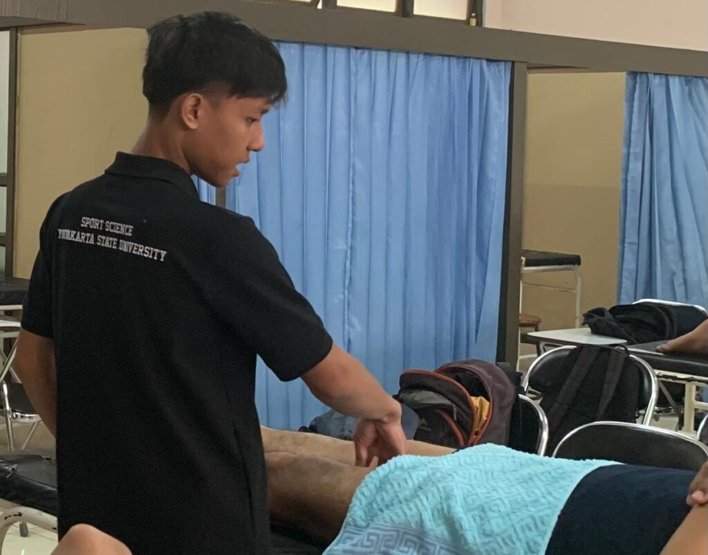 Whatsapp image 20260616 at 11 09 01 catrawarta Male practitioner in a black polo performs a massage on a person lying on a treatment table blue towel over them in a room with blue curtains and equipment nearby
